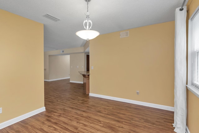 spare room with dark wood-style floors, a textured ceiling, visible vents, and baseboards