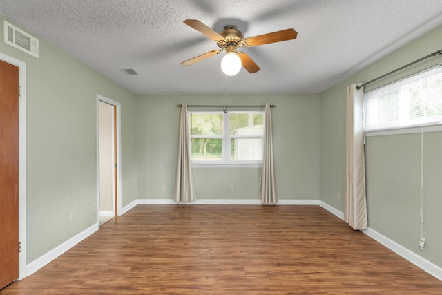 unfurnished room featuring visible vents, a textured ceiling, baseboards, and wood finished floors