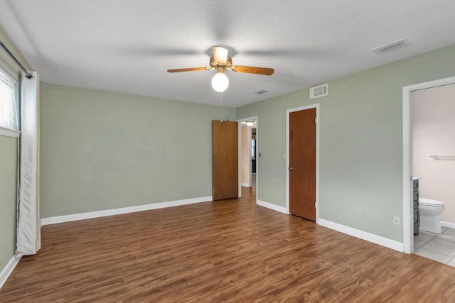 unfurnished bedroom with a textured ceiling, wood finished floors, visible vents, and baseboards