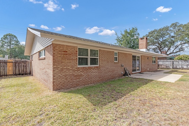 rear view of property featuring a patio, a chimney, fence, a yard, and brick siding