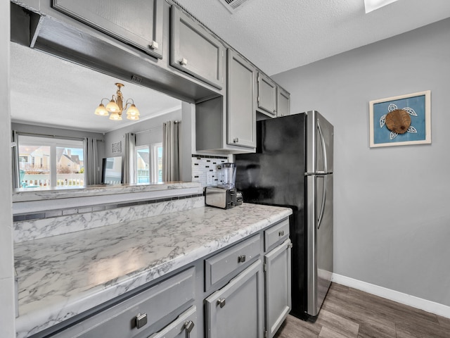 kitchen featuring a notable chandelier, gray cabinetry, dark wood-type flooring, baseboards, and backsplash