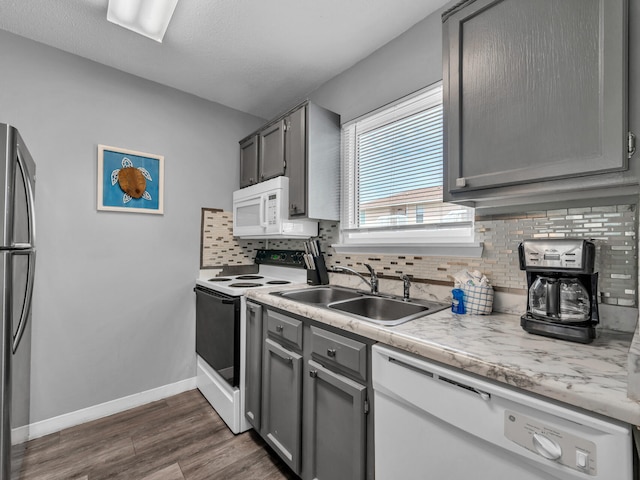 kitchen featuring dark wood-style flooring, decorative backsplash, gray cabinetry, a sink, and white appliances