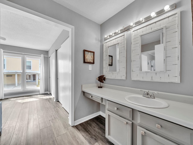 bathroom with a textured ceiling, baseboards, wood finished floors, and vanity