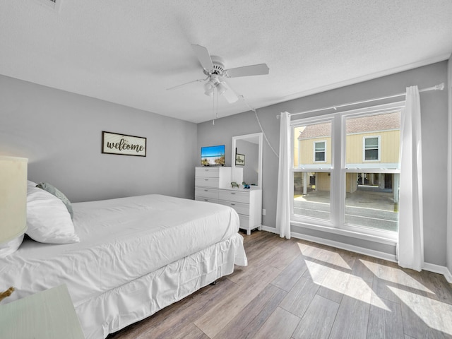 bedroom with baseboards, a textured ceiling, a ceiling fan, and wood finished floors