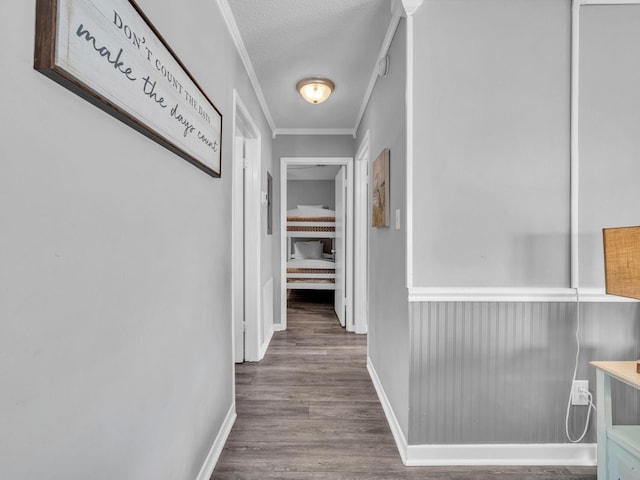 hallway with crown molding, a textured ceiling, baseboards, and wood finished floors