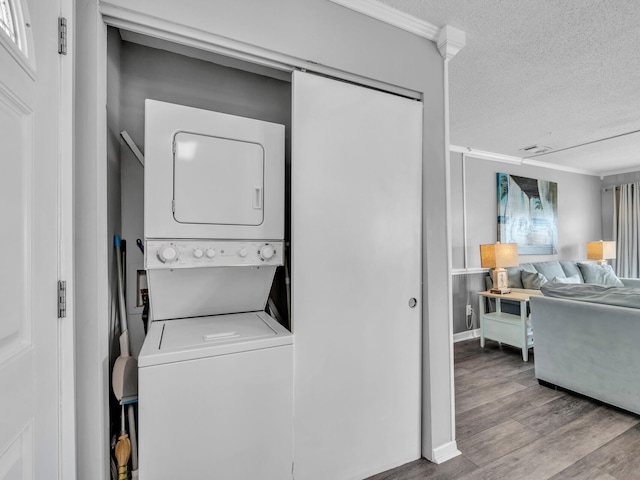 laundry area featuring laundry area, visible vents, stacked washer / drying machine, wood finished floors, and a textured ceiling