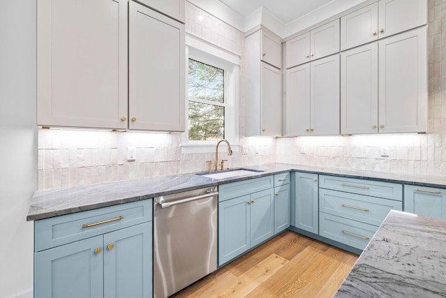 kitchen featuring light wood finished floors, tasteful backsplash, light stone counters, stainless steel dishwasher, and a sink