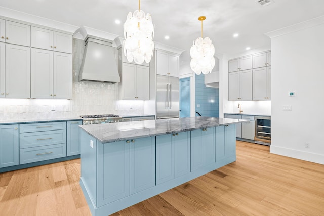 kitchen featuring beverage cooler, built in refrigerator, a kitchen island, decorative light fixtures, and custom range hood