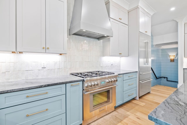 kitchen featuring white cabinets, high end appliances, light wood-style flooring, custom range hood, and light stone countertops