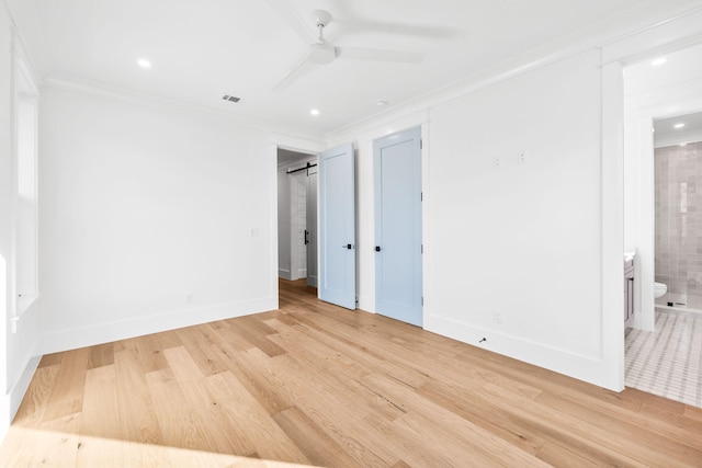 unfurnished bedroom with ornamental molding, a barn door, light wood-style flooring, and baseboards