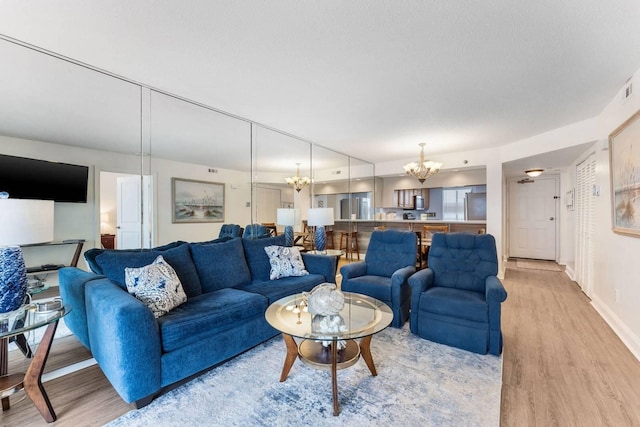 living area with light wood-style floors, a textured ceiling, baseboards, and an inviting chandelier