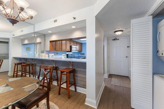 kitchen featuring stacked washer and clothes dryer, pendant lighting, visible vents, brown cabinetry, and a peninsula