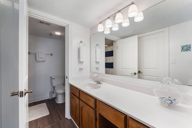 bathroom featuring visible vents, toilet, vanity, a textured ceiling, and wood finished floors