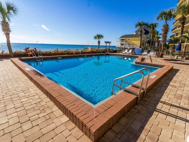 community pool with a patio area, a water view, and fence