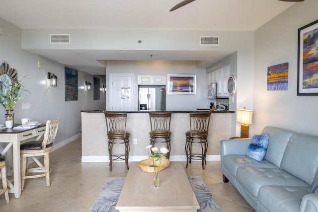 living room with light tile patterned floors, baseboards, visible vents, and ceiling fan