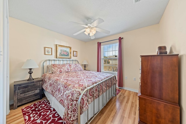 bedroom featuring ceiling fan, light wood-style flooring, baseboards, and a textured ceiling