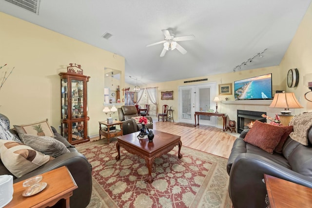 living room featuring light wood-type flooring, visible vents, vaulted ceiling, and a tile fireplace