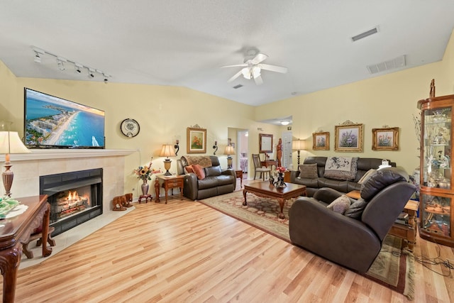 living area with a ceiling fan, a tiled fireplace, visible vents, and light wood-style floors