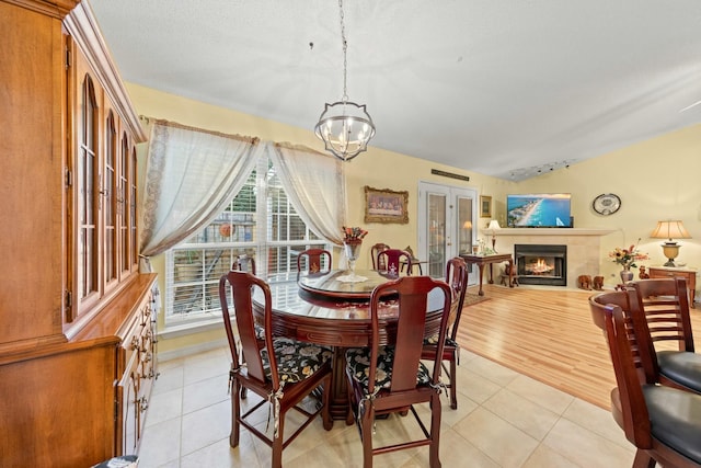 dining area with vaulted ceiling, french doors, a warm lit fireplace, and light tile patterned flooring