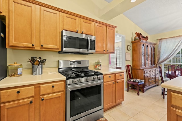 kitchen with lofted ceiling, stainless steel appliances, light countertops, and brown cabinets