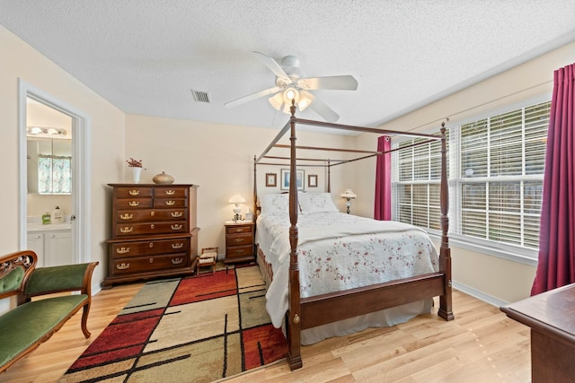 bedroom with light wood finished floors, connected bathroom, visible vents, and a textured ceiling