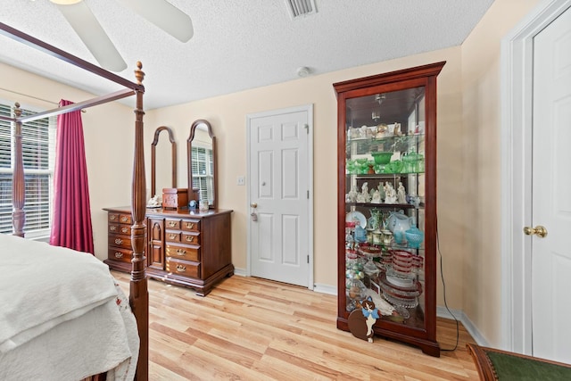 bedroom featuring light wood-type flooring, visible vents, a textured ceiling, and baseboards