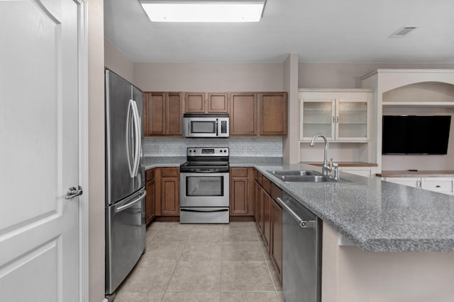 kitchen featuring light tile patterned floors, appliances with stainless steel finishes, brown cabinets, and a sink