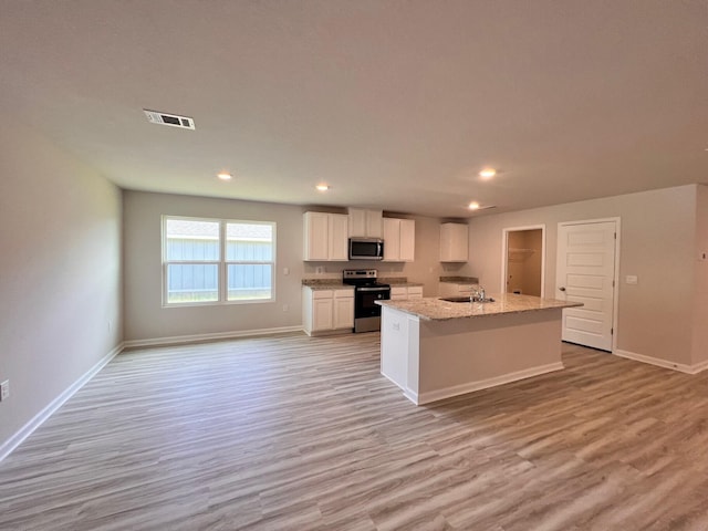 kitchen featuring visible vents, appliances with stainless steel finishes, light stone counters, a kitchen island with sink, and white cabinetry