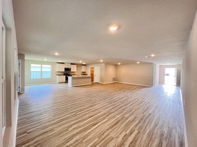 unfurnished living room with baseboards, a textured ceiling, recessed lighting, and light wood-style floors