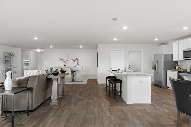 kitchen with white cabinetry, appliances with stainless steel finishes, dark wood-style floors, an island with sink, and a kitchen bar