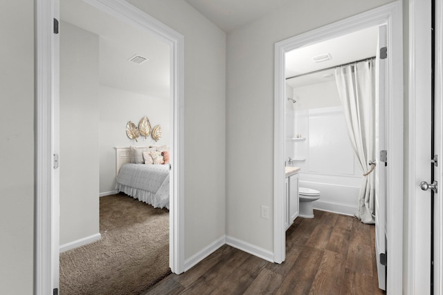 hall featuring dark colored carpet, visible vents, dark wood finished floors, and baseboards