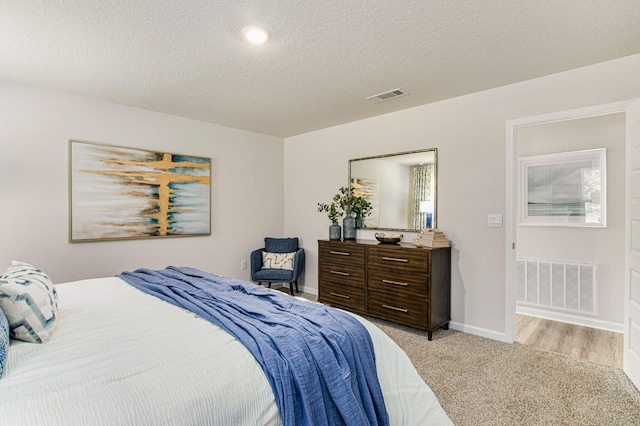 bedroom featuring light carpet, baseboards, visible vents, and a textured ceiling