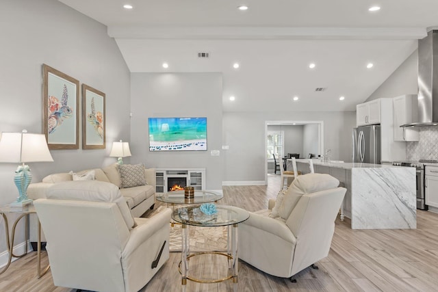 living area featuring light wood finished floors, a glass covered fireplace, beam ceiling, and visible vents