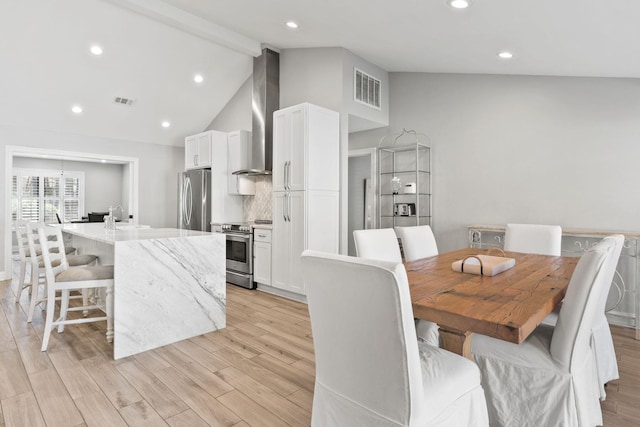 dining space featuring visible vents, light wood-style floors, and vaulted ceiling with beams