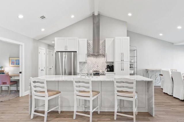 kitchen with light stone counters, a spacious island, white cabinetry, freestanding refrigerator, and wall chimney exhaust hood