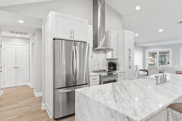 kitchen with visible vents, stainless steel appliances, light wood-style floors, white cabinetry, and wall chimney exhaust hood