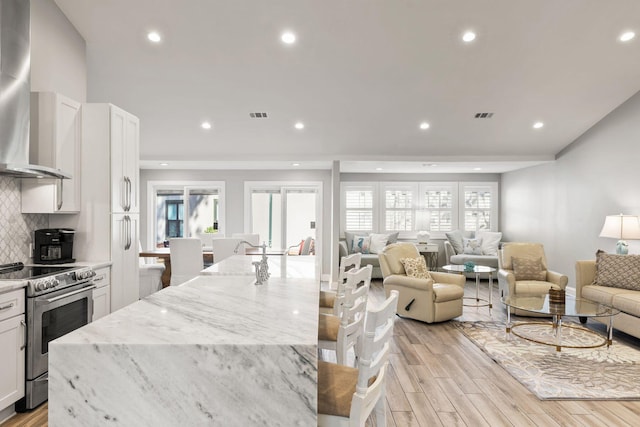 kitchen with light wood finished floors, electric stove, backsplash, a spacious island, and wall chimney range hood