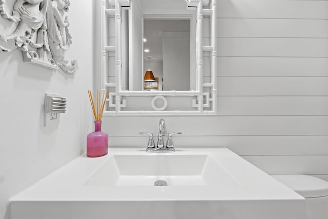 bathroom with a sink, wooden walls, and toilet