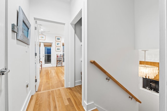 hallway with an upstairs landing, a notable chandelier, and light wood finished floors