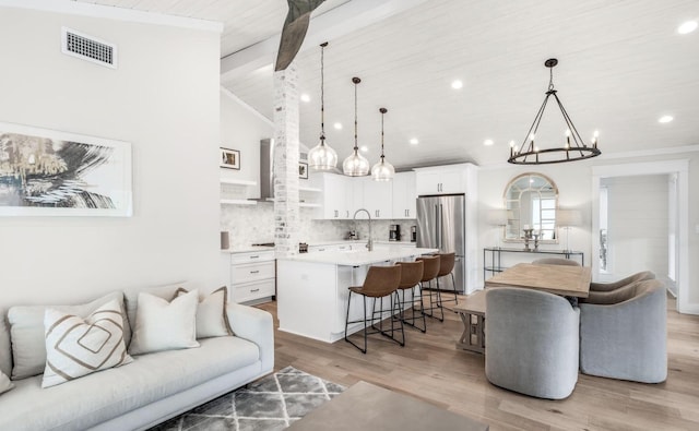 kitchen featuring freestanding refrigerator, light countertops, hanging light fixtures, and a kitchen island with sink