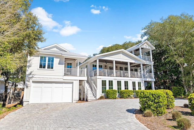 view of front facade featuring decorative driveway, an attached garage, board and batten siding, a balcony, and stairs