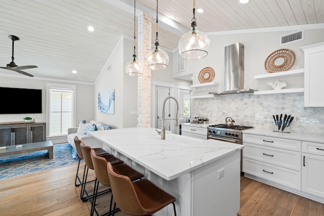 kitchen with decorative light fixtures, visible vents, white cabinets, an island with sink, and wall chimney exhaust hood