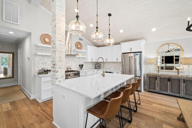 kitchen featuring visible vents, high end appliances, wall chimney exhaust hood, light stone countertops, and white cabinetry