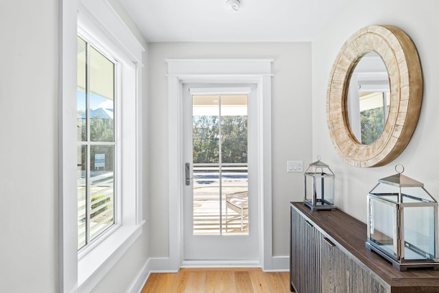 doorway with baseboards, a wealth of natural light, and light wood-style floors