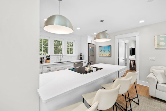 kitchen featuring pendant lighting, light countertops, appliances with stainless steel finishes, white cabinetry, and a sink