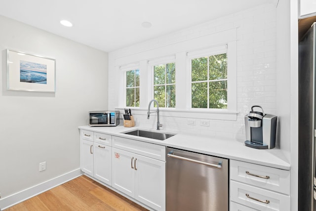 kitchen with appliances with stainless steel finishes, white cabinets, light countertops, and a sink