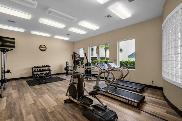 exercise room with baseboards, visible vents, and wood finished floors