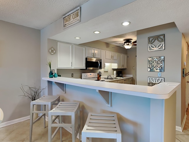 kitchen featuring a textured ceiling, a breakfast bar area, recessed lighting, light countertops, and stainless steel microwave