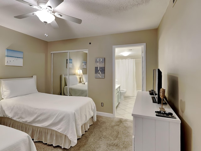 bedroom featuring a closet, light colored carpet, ensuite bathroom, a ceiling fan, and a textured ceiling