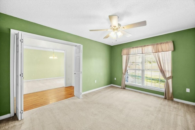 empty room featuring ceiling fan with notable chandelier, carpet floors, a textured ceiling, and baseboards